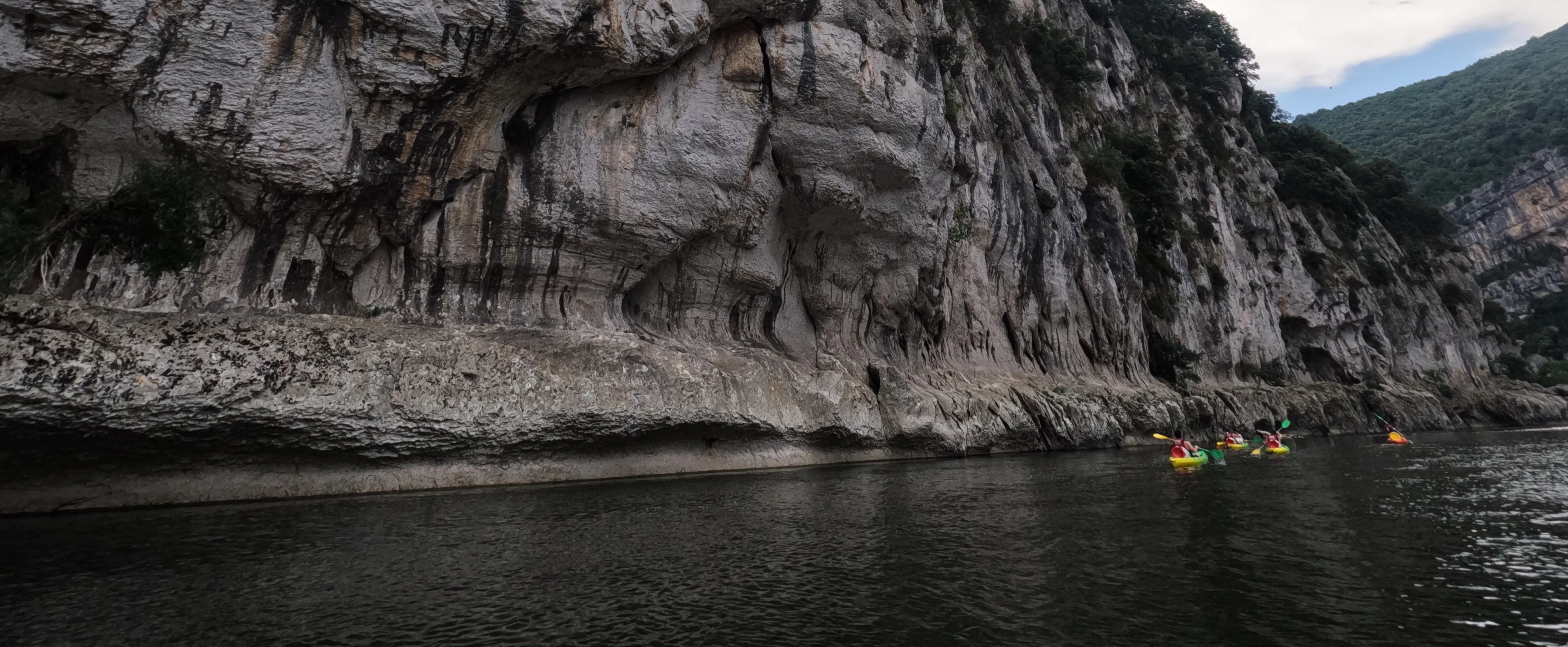 The Ardèche river, its rocky borders, four kayaks navigating it and an angle of sky.